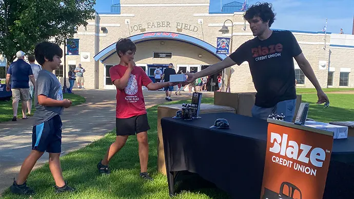 Blaze staff member handing a Rox fan Blaze merchandise in front of Joe Faber Field where the St. Cloud Rox play baseball